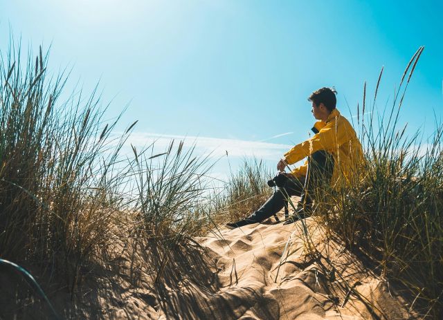 Mann sitzt in den Dünen am Strand; Wie soll ich 200.000 Euro anlegen? 