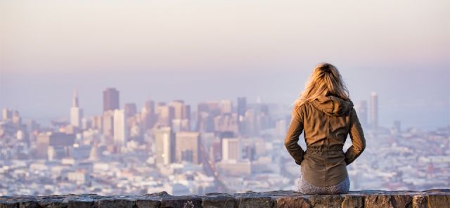 Das Bild zeigt eine Frau auf einer Mauer sitzend vor der Skyline einer Großstadt. ETF Depot.