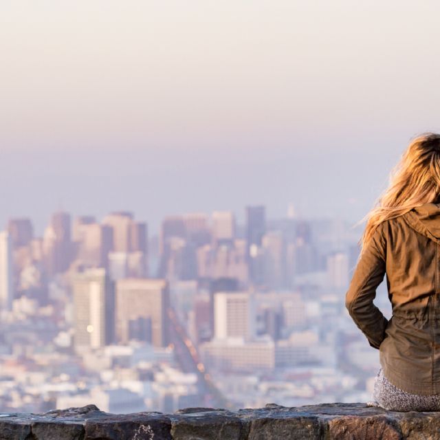 Das Bild zeigt eine Frau auf einer Mauer sitzend vor der Skyline einer Großstadt. ETF Depot.
