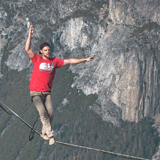 Ein mann balanciert auf einem Seil zwischen zwei Bergen.