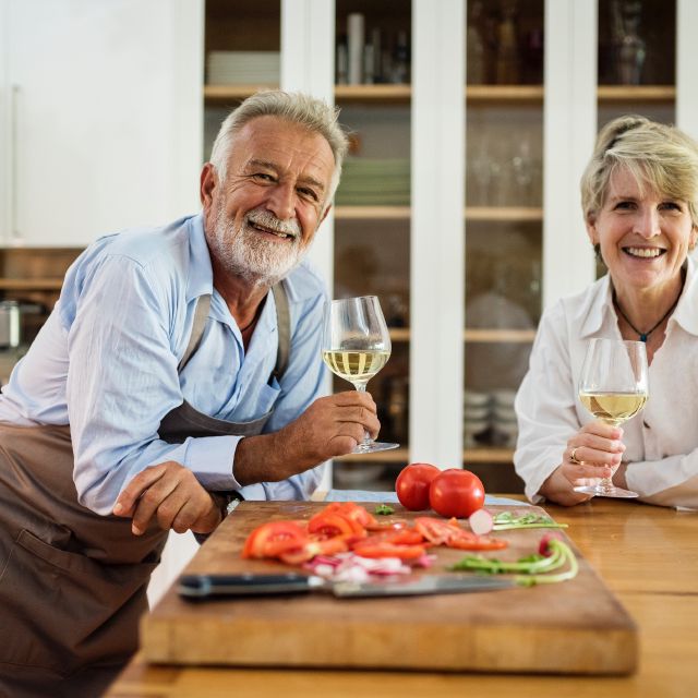 Ein älteres Ehepaar steht mit Wein in der Hand in der Küche.