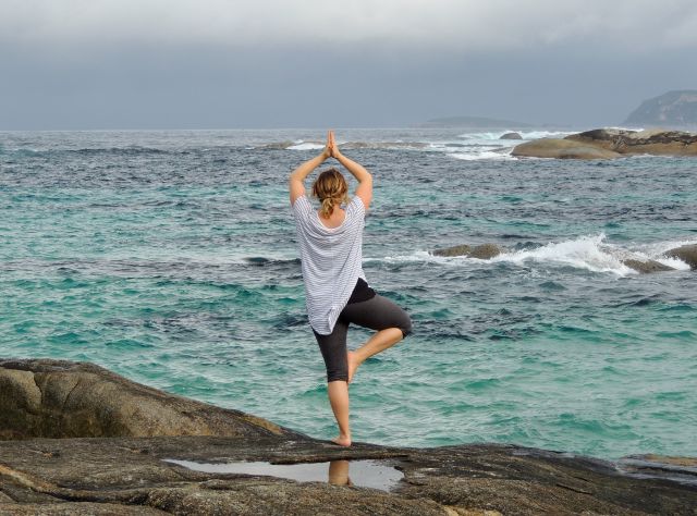 Eine Frau steht am Meer und macht eine Yoga Pose.