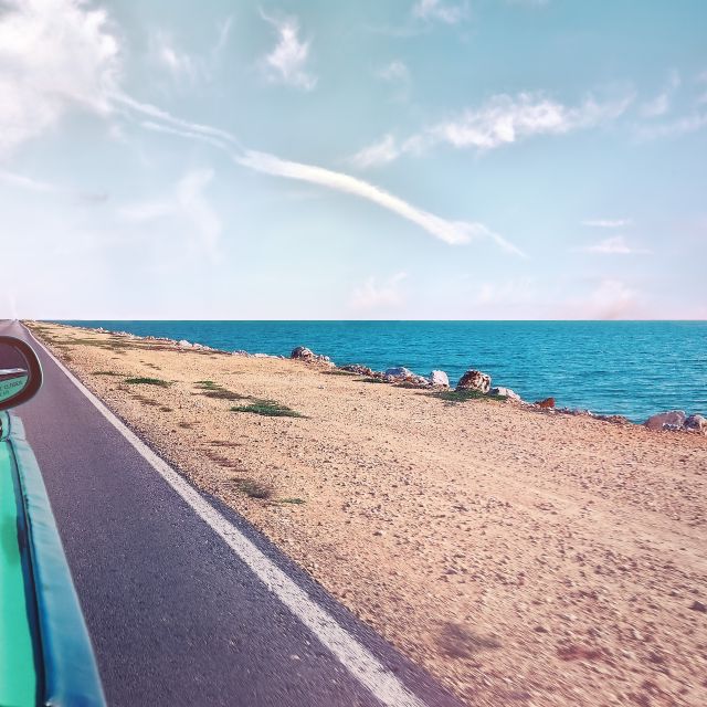 Das Bild zeigt die Seite eines Autos während es an einer Küstenstraße entlang fährt.