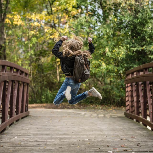 Ein Mädchen springt auf einer Brücke vor Freude in die Luft.