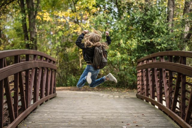 Ein Mädchen springt auf einer Brücke vor Freude in die Luft.