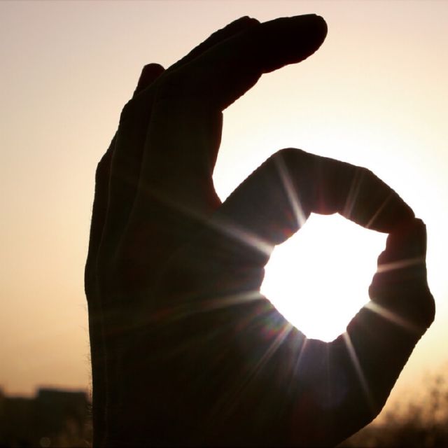 Das Bild zeigt eine Kreis-machende Hand vor einem Sonnenuntergang.