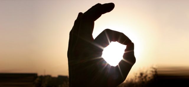 Das Bild zeigt eine Kreis-machende Hand vor einem Sonnenuntergang.